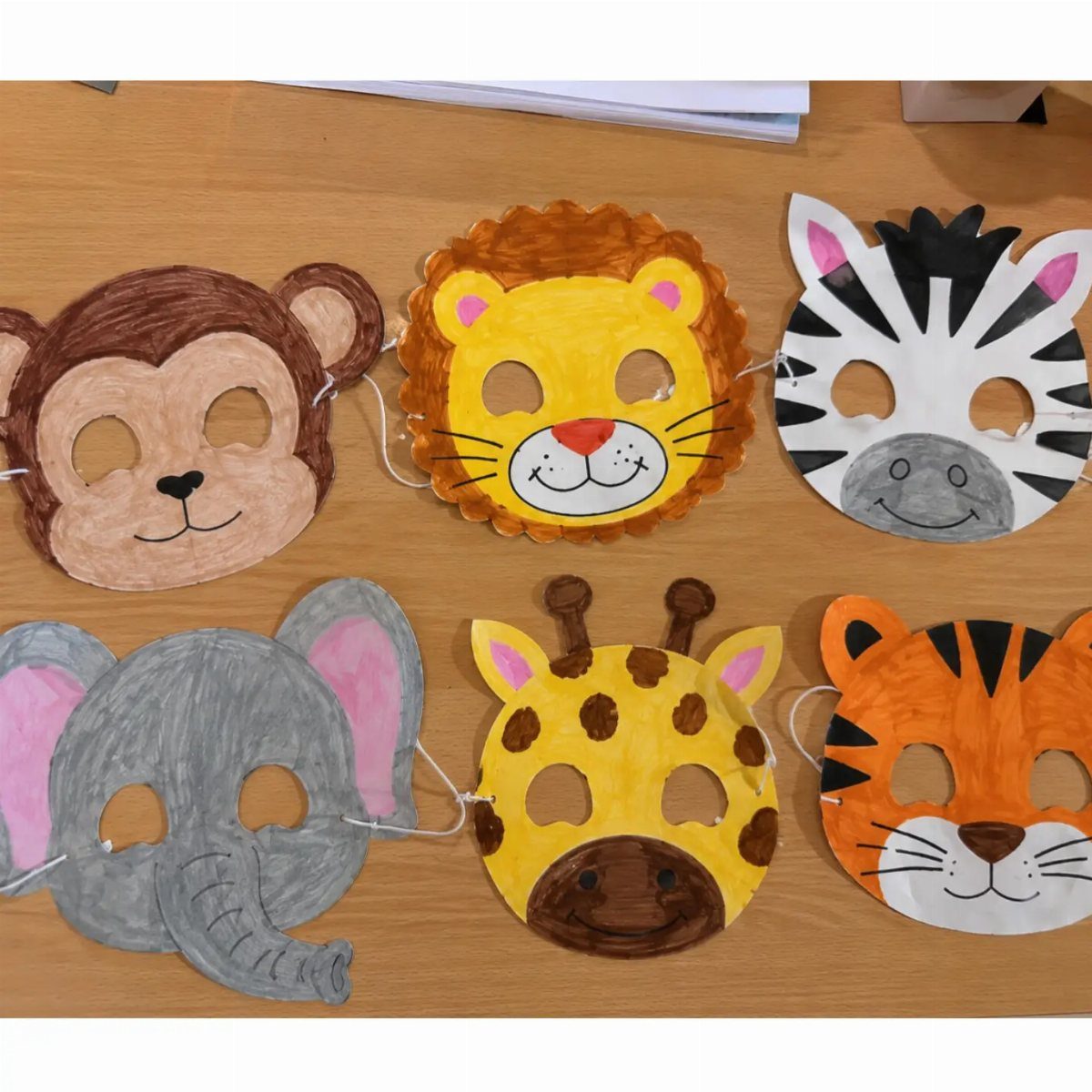 Handmade animal masks made from paper plates on a wooden table.