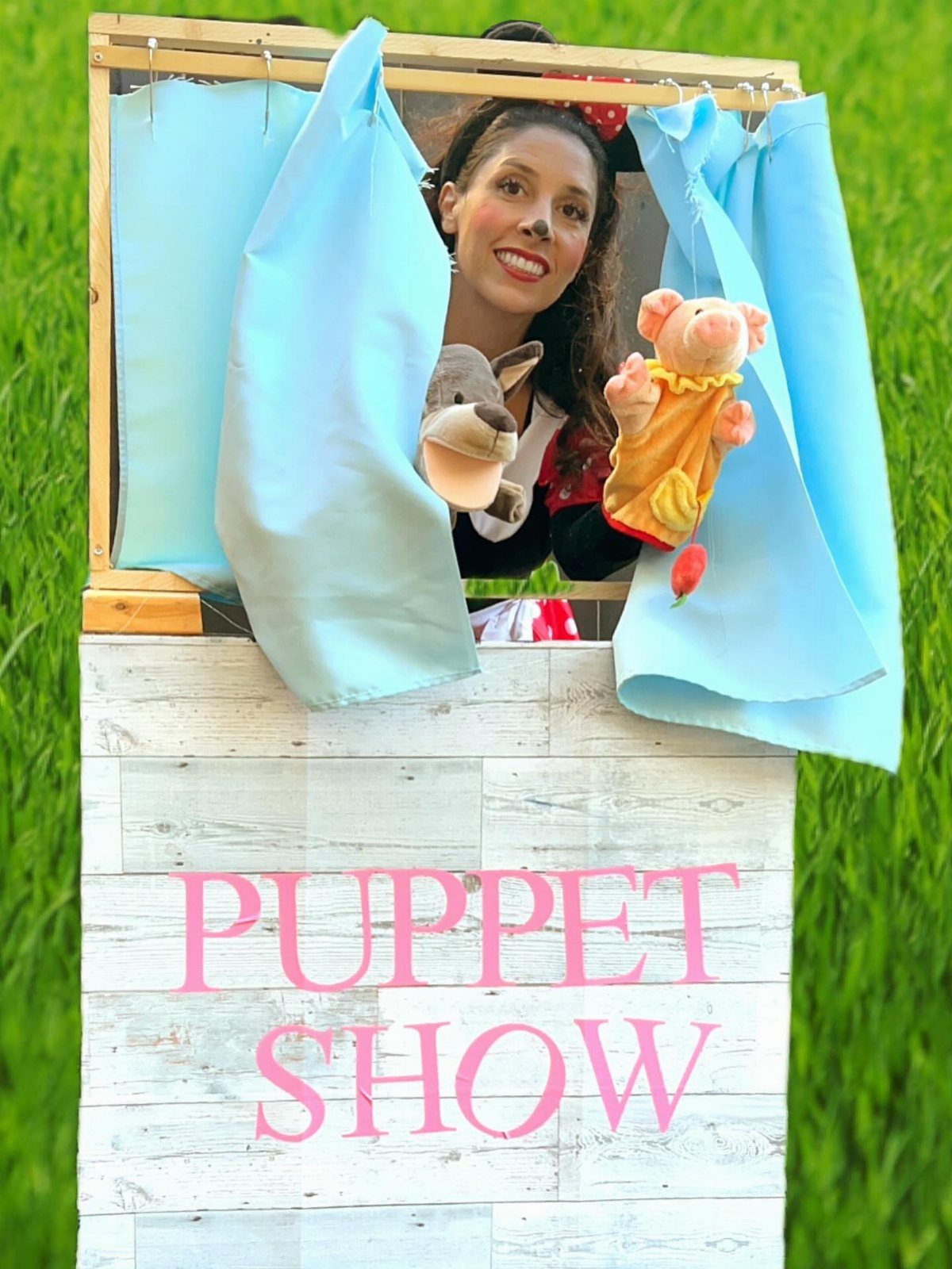 Woman performing a puppet show behind a wooden theater with blue curtains.