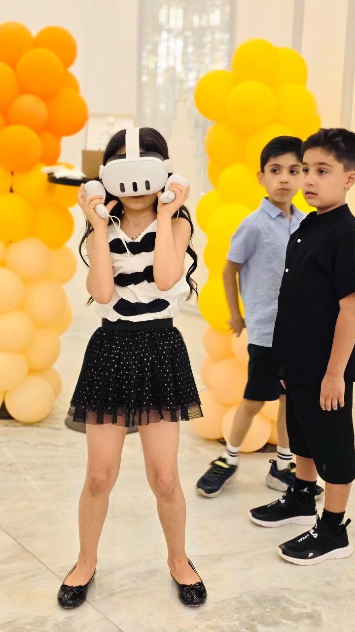 Girl wearing a VR headset and holding controllers with boys watching nearby.