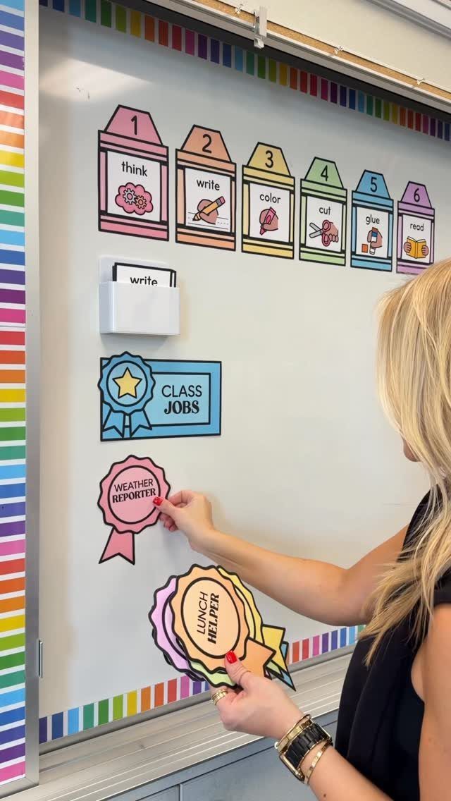 Woman placing colorful class job ribbons on a whiteboard with rainbow borders.