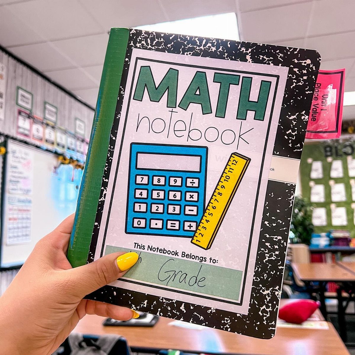 Composition notebook with math graphics held by a hand in a classroom setting.