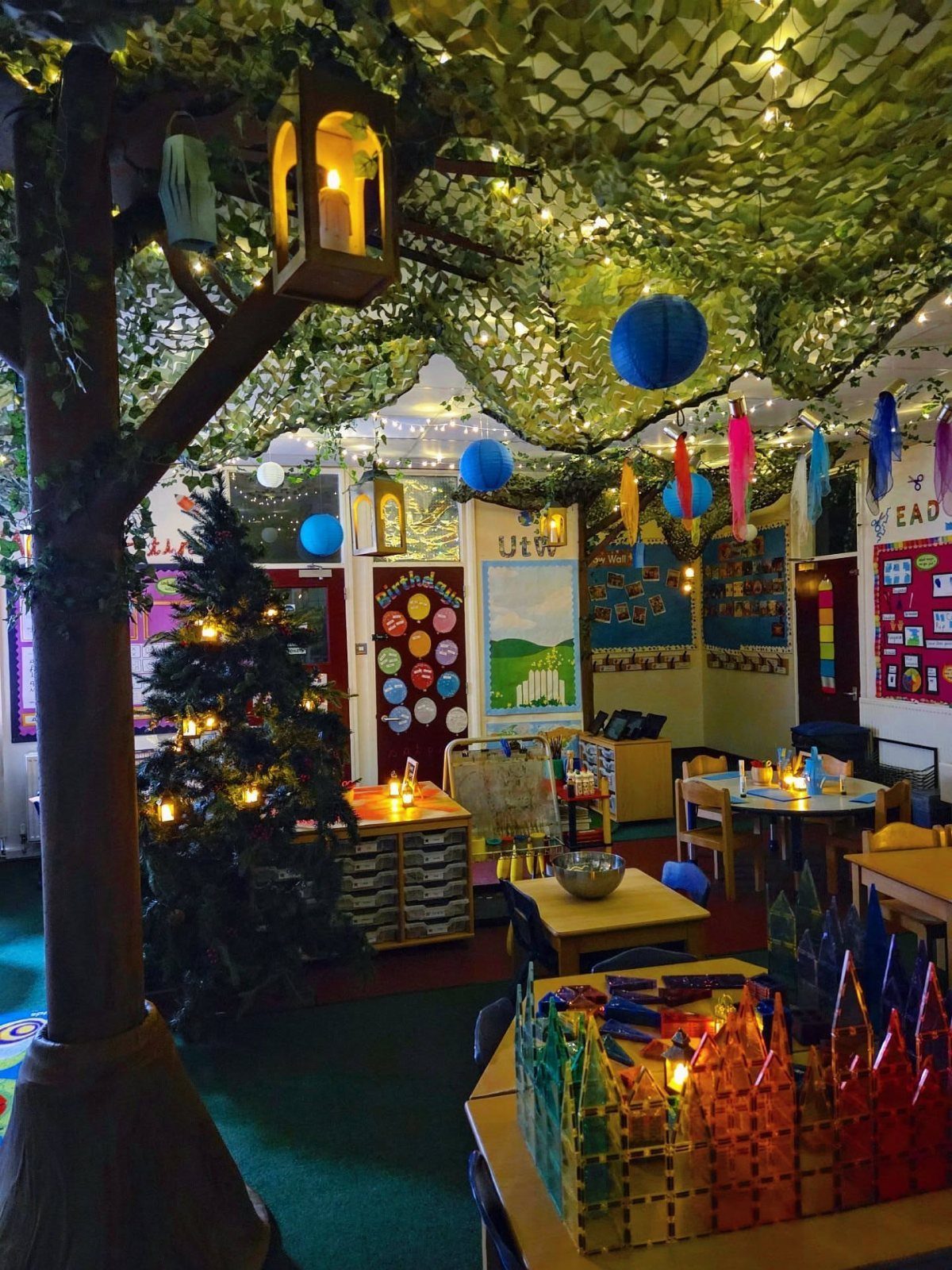 Magical forest classroom theme with a large artificial tree and twinkling fairy lights.