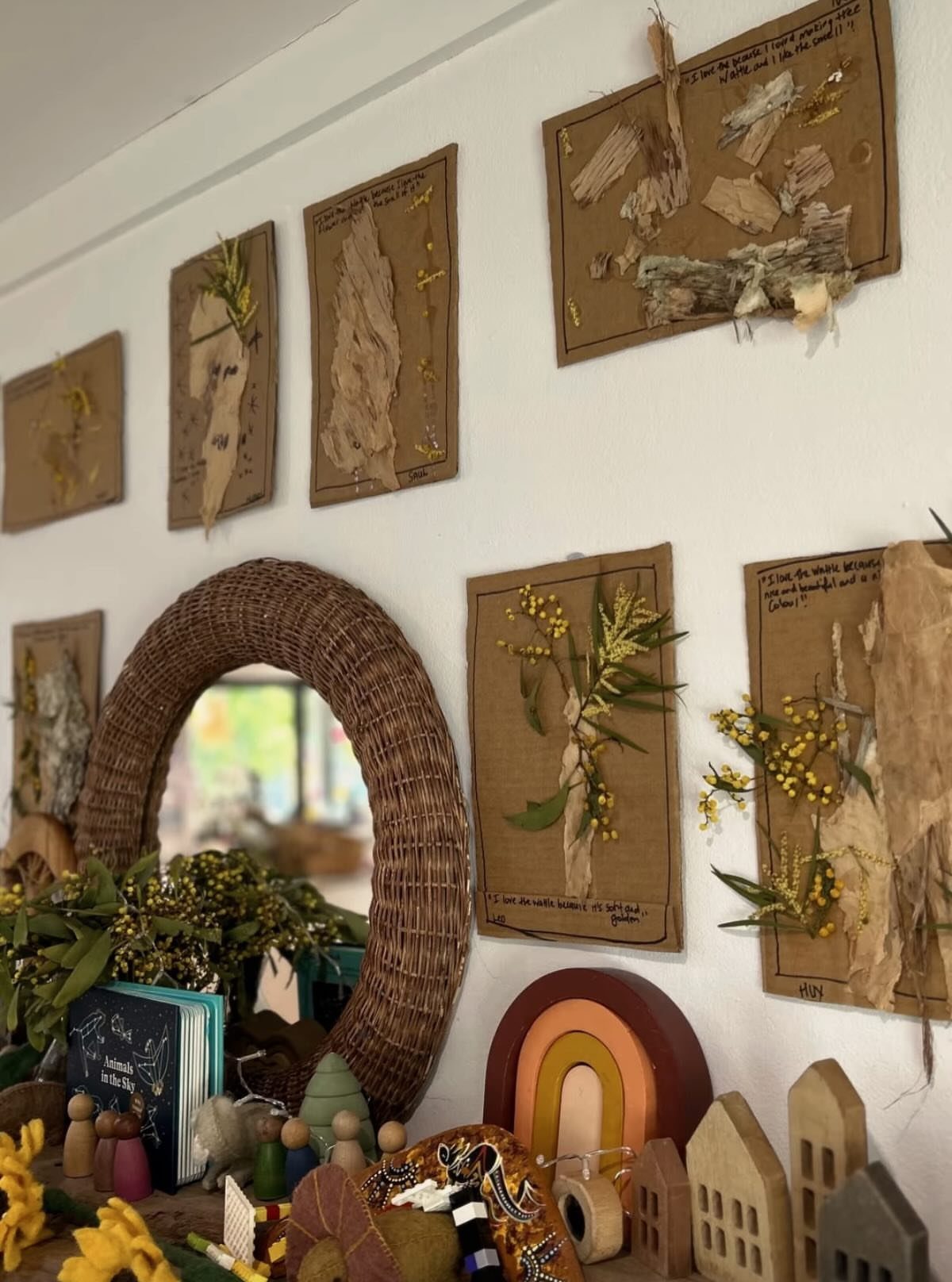 Nature-themed classroom wall with dried plant displays, a woven mirror, and wooden toys.