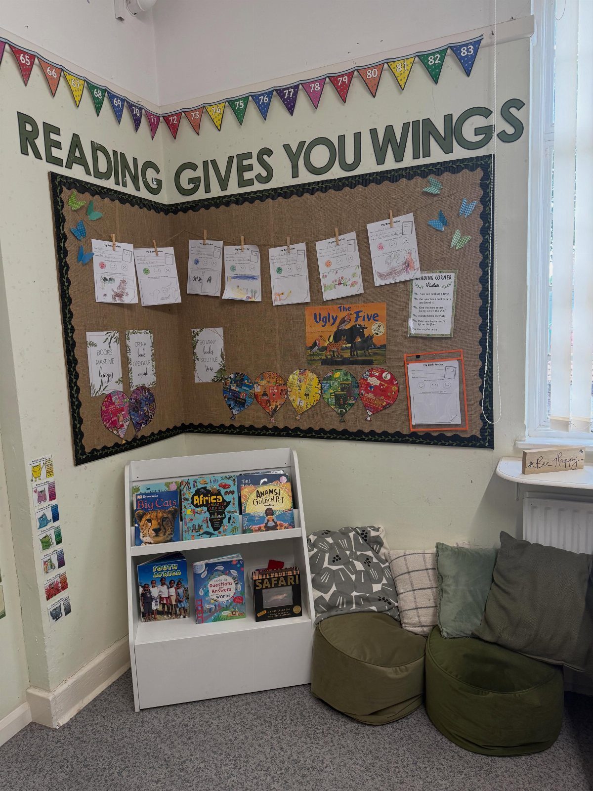 Reading nook with a themed bulletin board, white bookshelf, and green beanbag chairs.