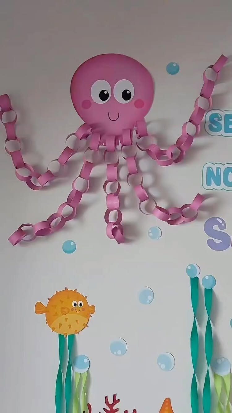 Pink paper octopus and yellow fish decorations on a white classroom wall.