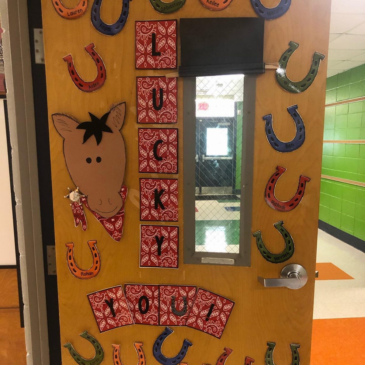 Wooden classroom door decorated with a cartoon horse and colorful horseshoe cutouts.