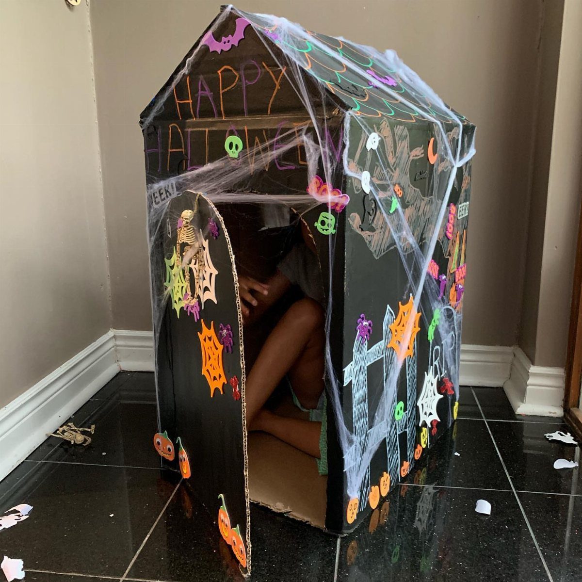 Black cardboard haunted house decorated with colorful drawings and white spider webs.