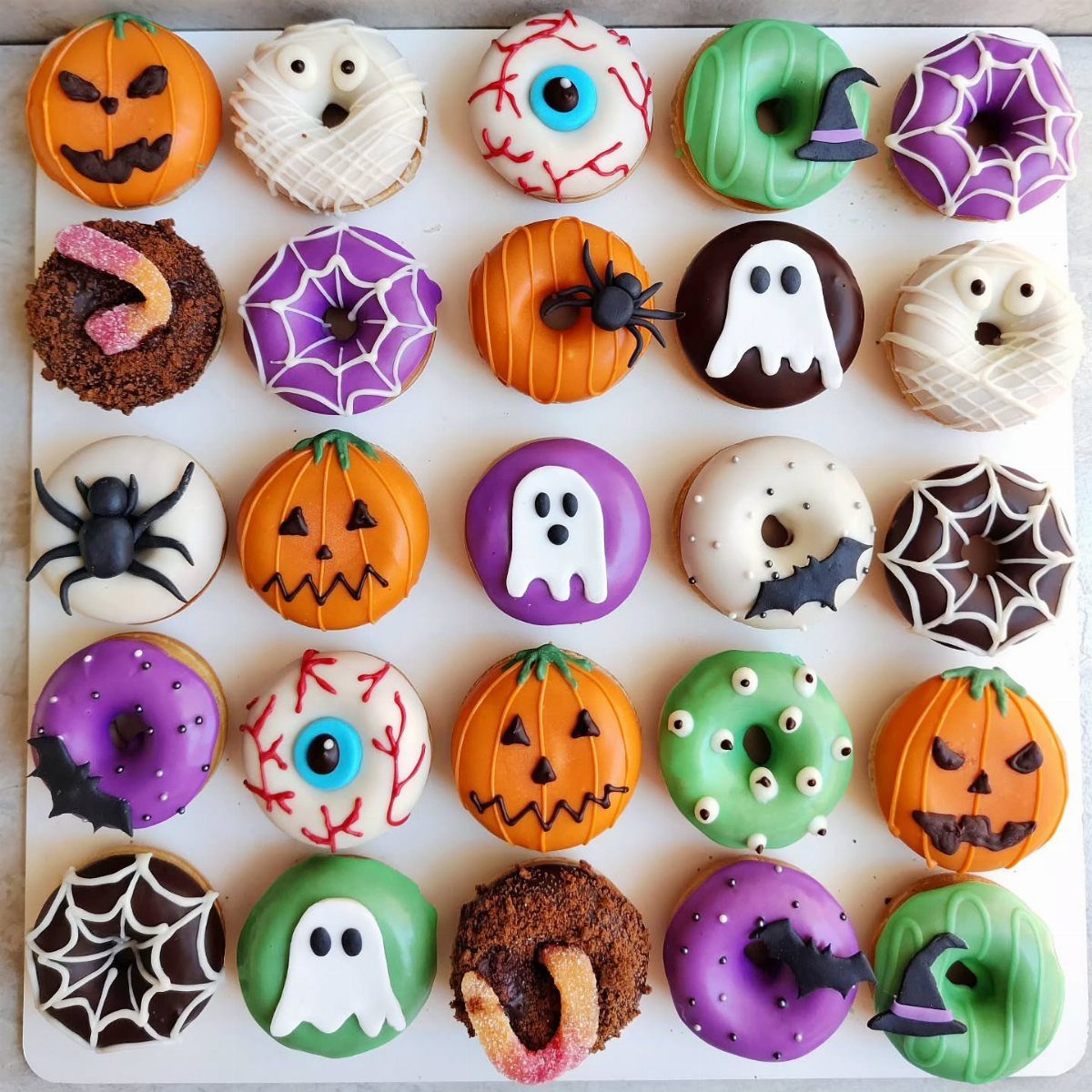 Halloween-themed doughnuts decorated as pumpkins, ghosts, and eyeballs on a white tray.