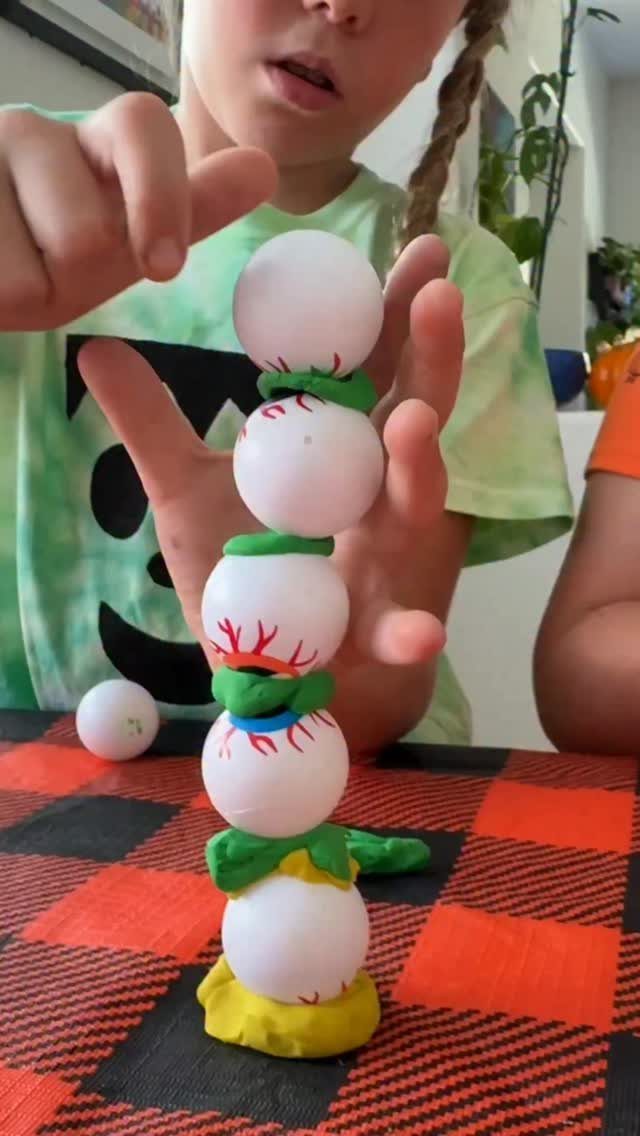 Child holding a stack of eyeball-painted ping pong balls held by colorful clay.