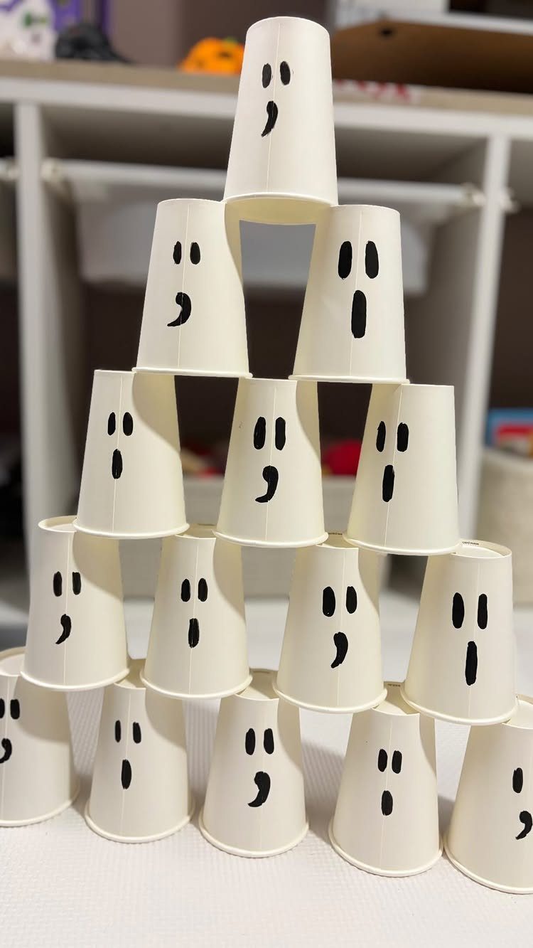 White paper cups with ghost faces stacked in a pyramid for bowling.