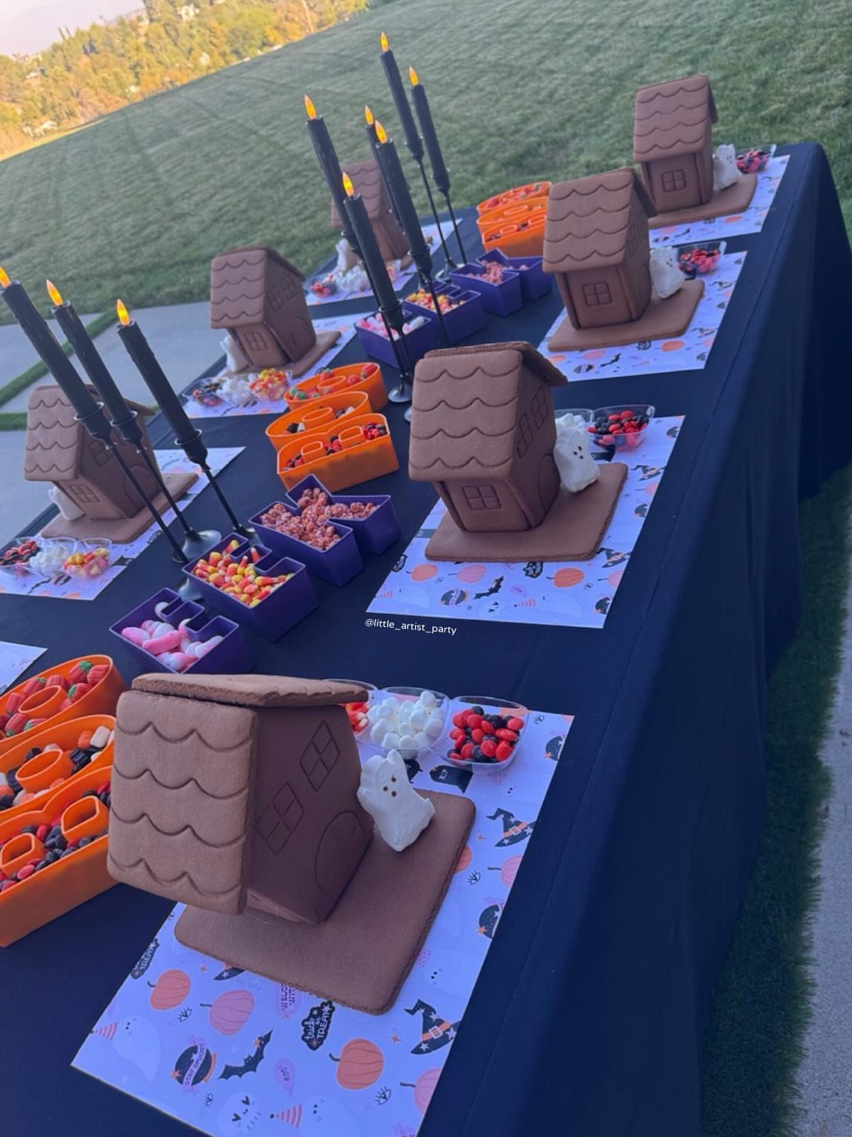 Graham cracker haunted houses on a decorated party table with candy and candles.