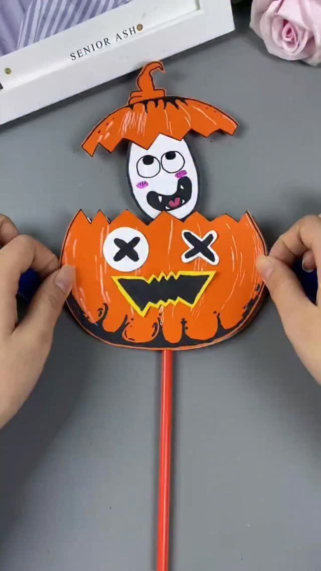 Paper craft of a ghost popping out of an orange pumpkin on a stick