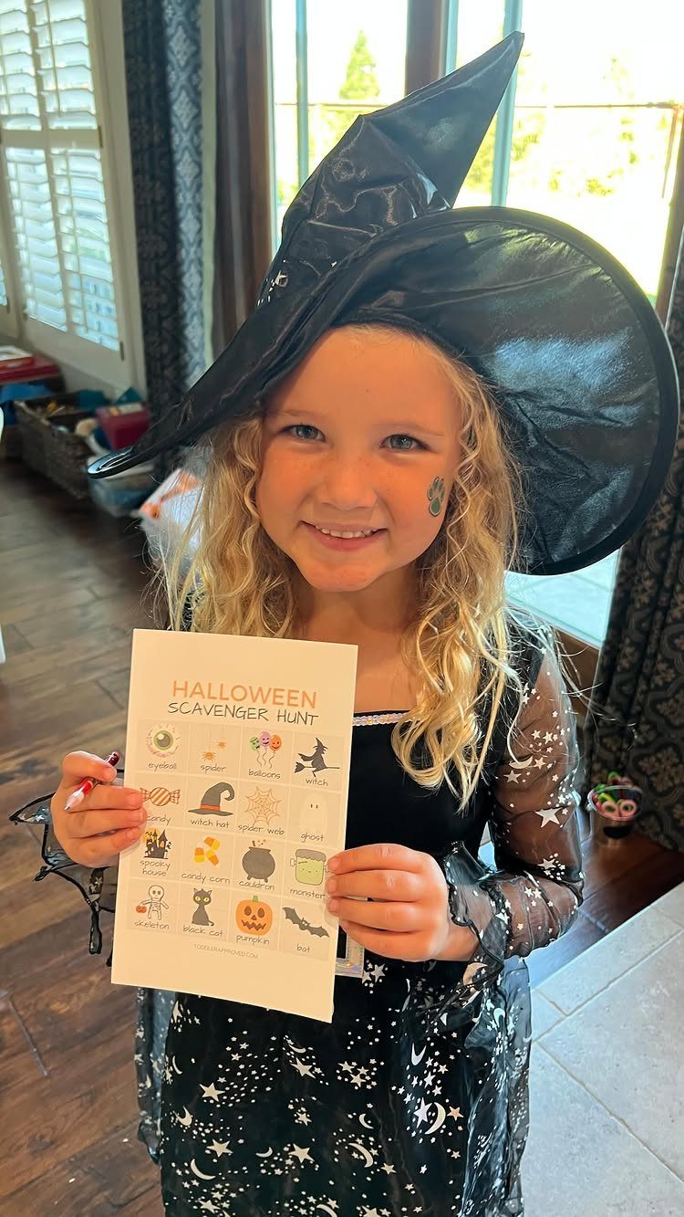Young girl in a witch costume holding a Halloween scavenger hunt checklist.