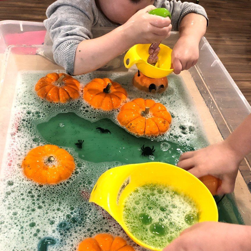Children playing with pumpkins and spiders in a green bubbly sensory bin.