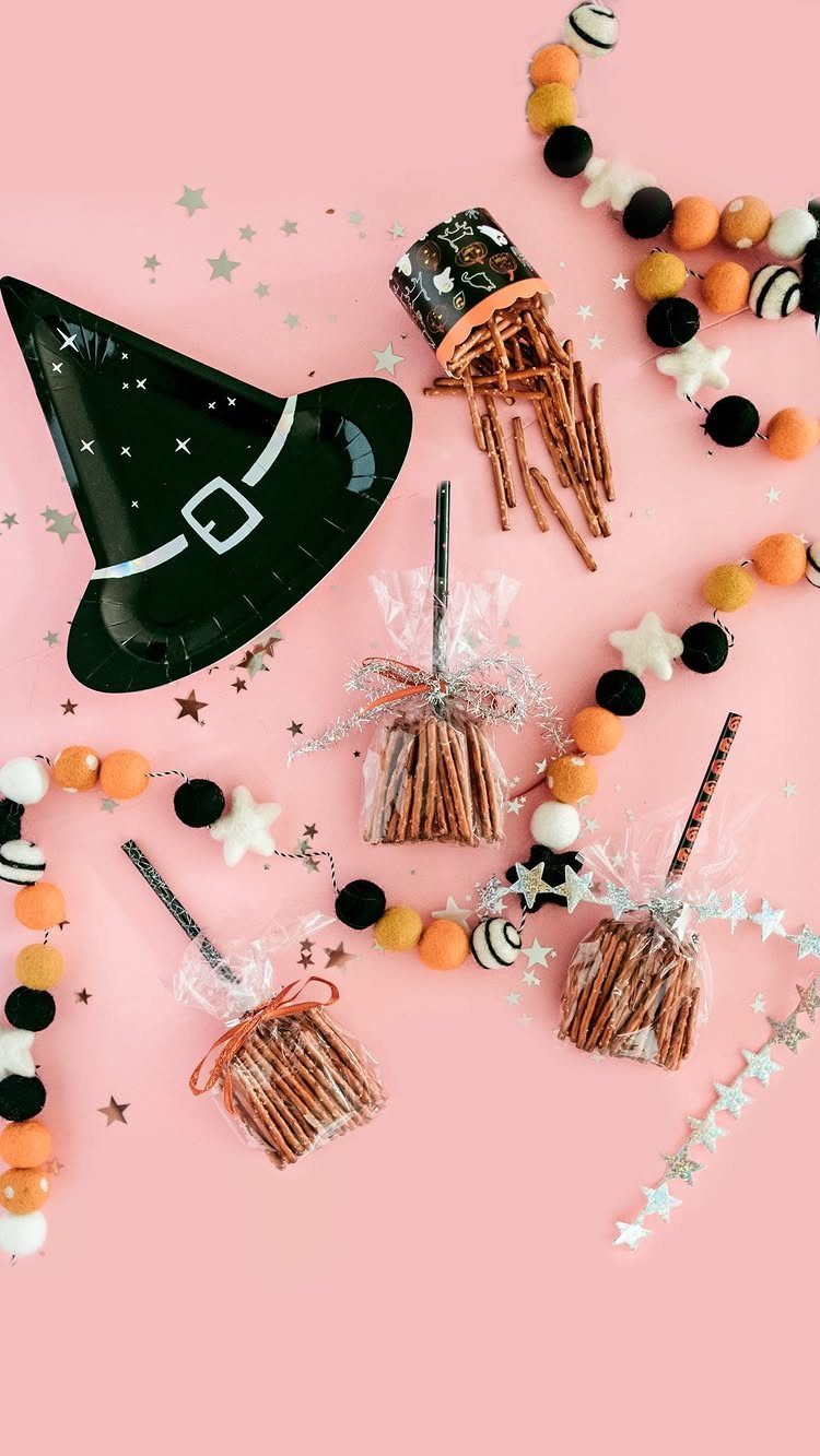 Miniature pretzel broomsticks and a witch hat plate on a pink background.