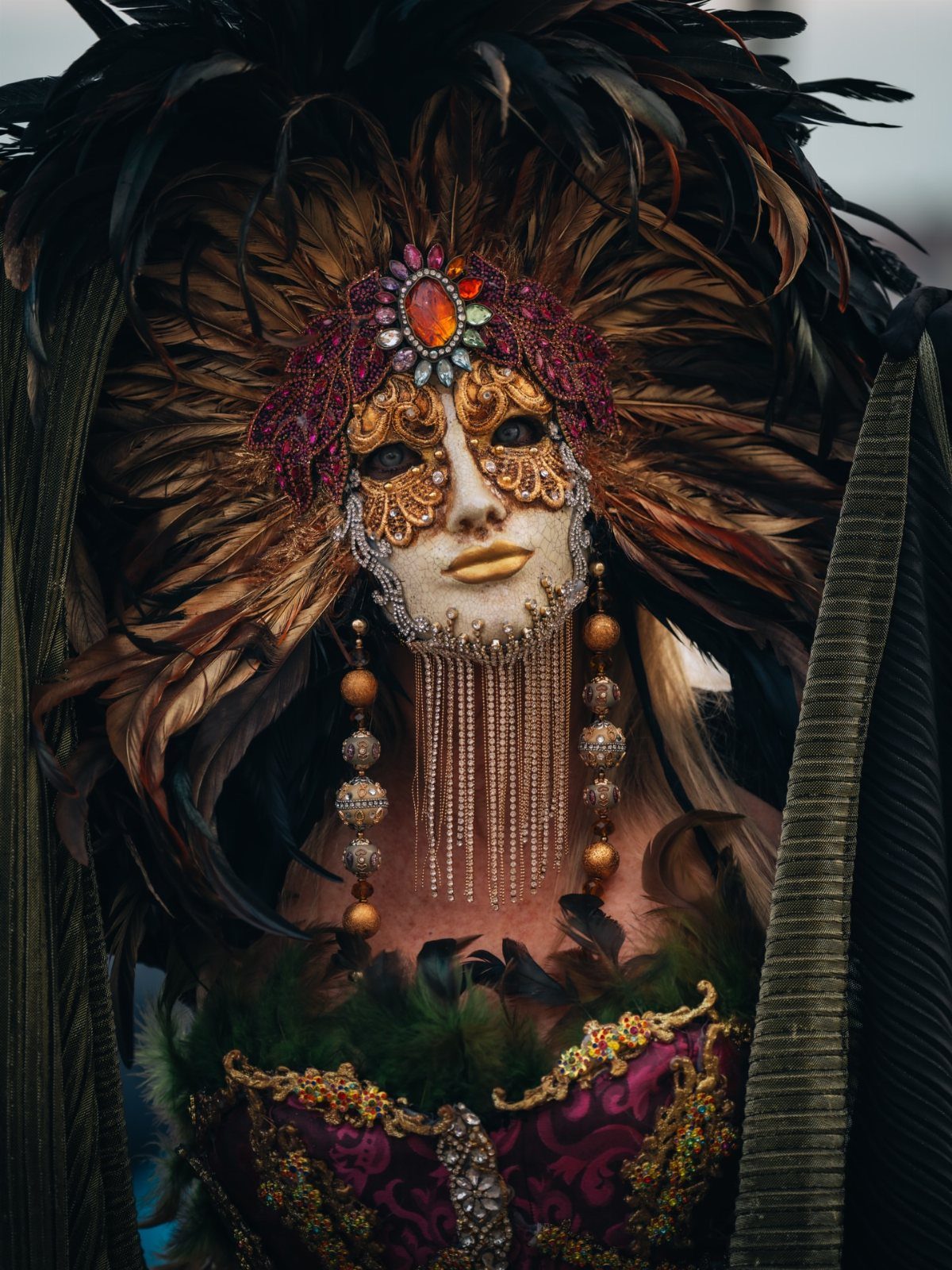 Person in an ornate gold masquerade mask with large feathers and purple bodice