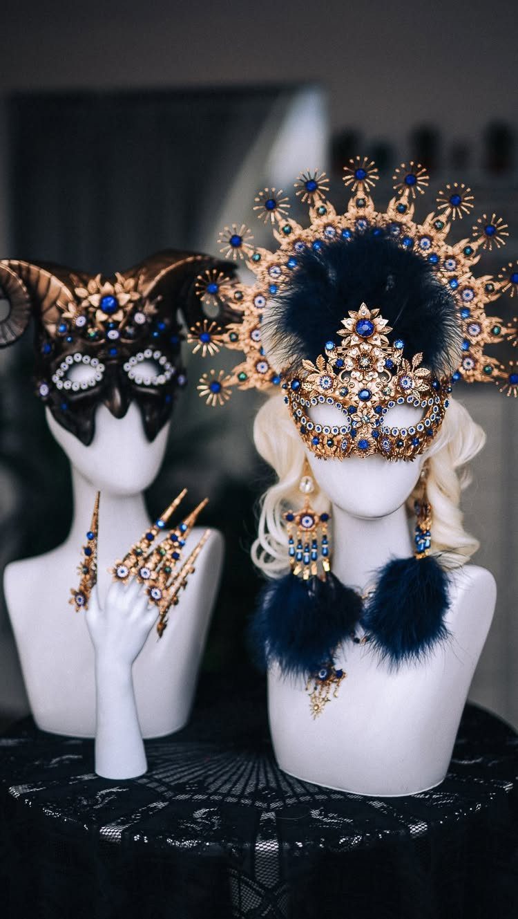Ornate gold and black masquerade masks with blue gems on white mannequins.