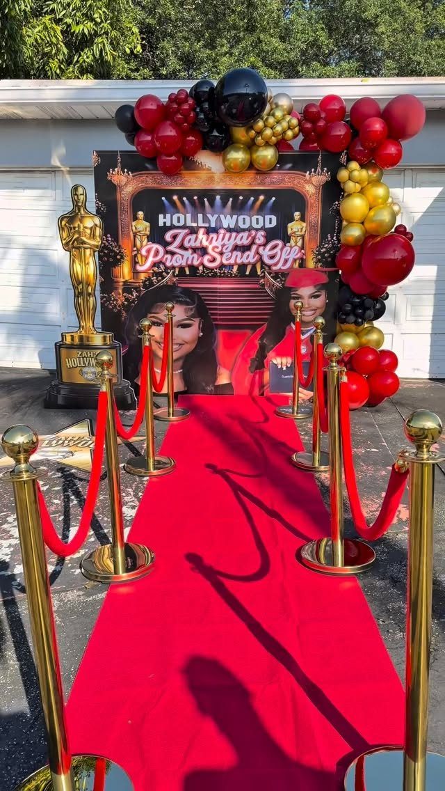 Red carpet walkway with gold stanchions and velvet ropes leading to a Hollywood backdrop.