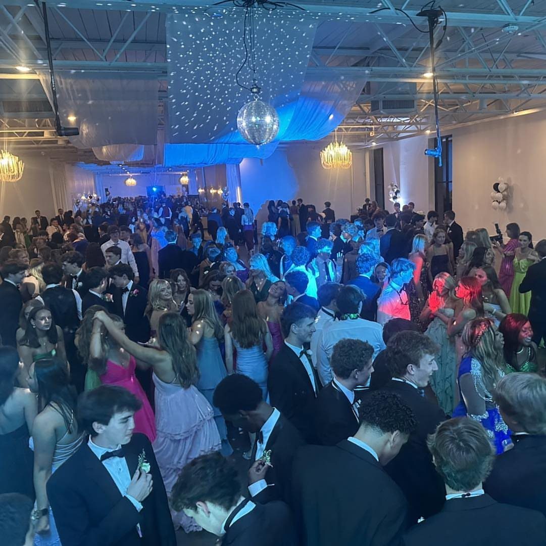 Teenagers dancing at a prom with deep blue lighting and star projections overhead.