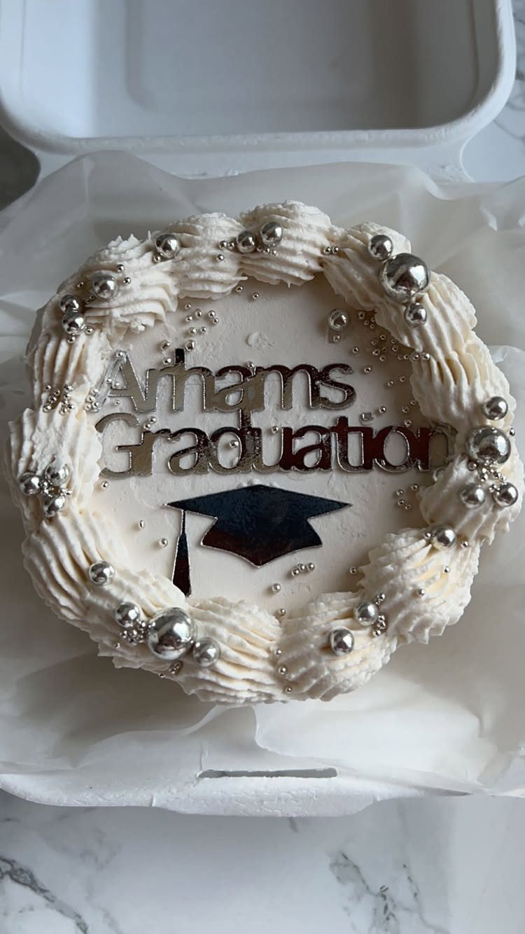 White graduation cake with silver pearls and a graduation cap cake topper.