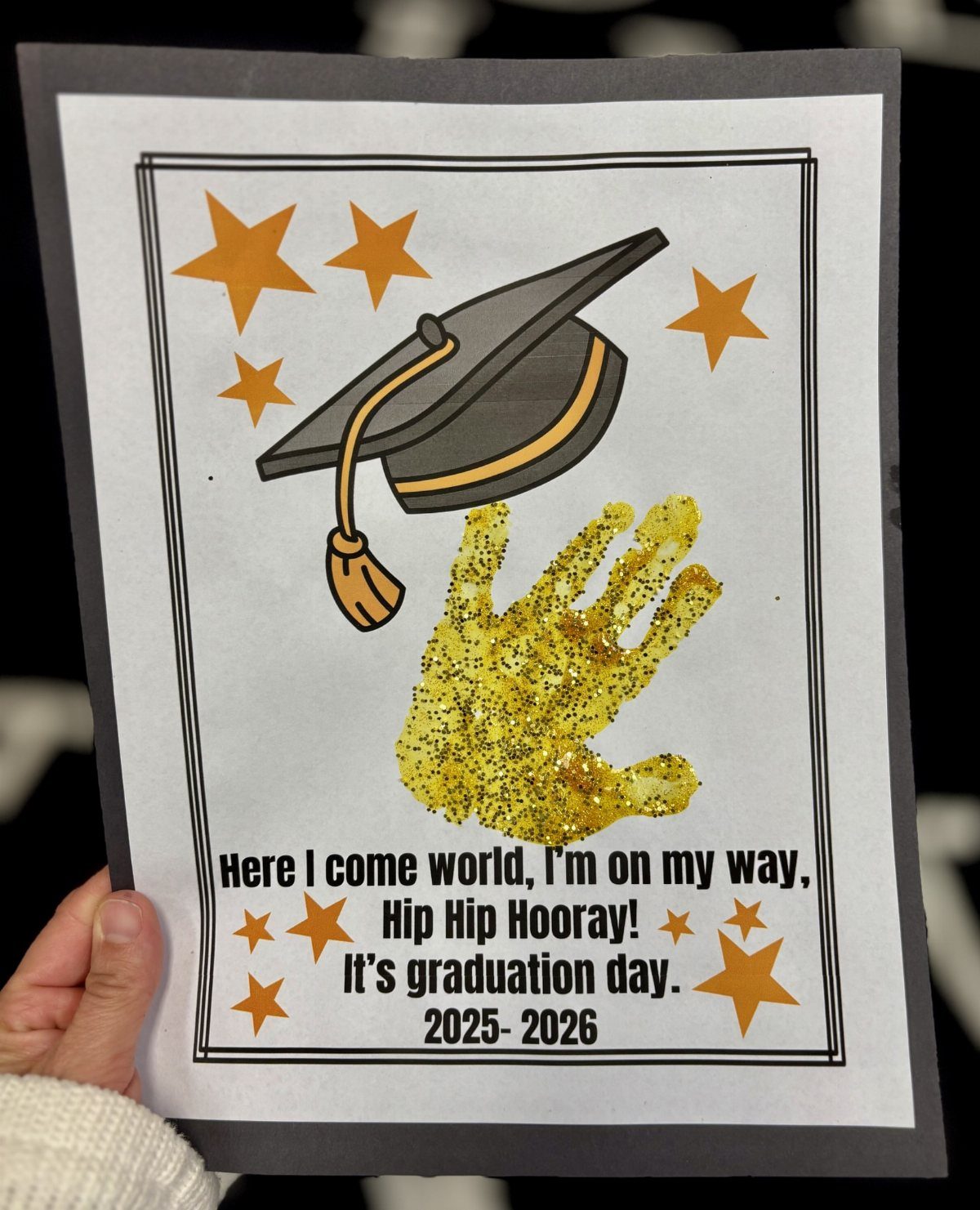 Graduation invitation featuring a gold glittery child's handprint and a graduation cap.