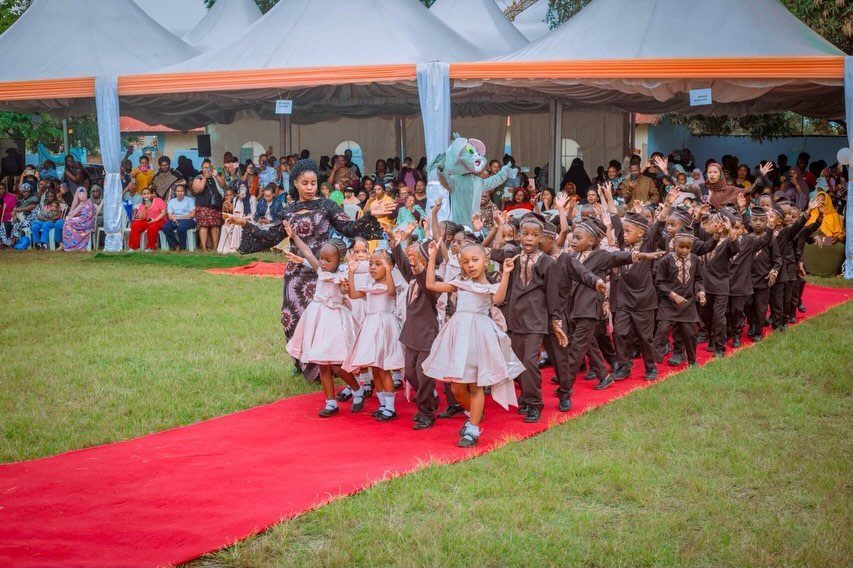 Children in formal wear walking down a red carpet during a graduation ceremony.