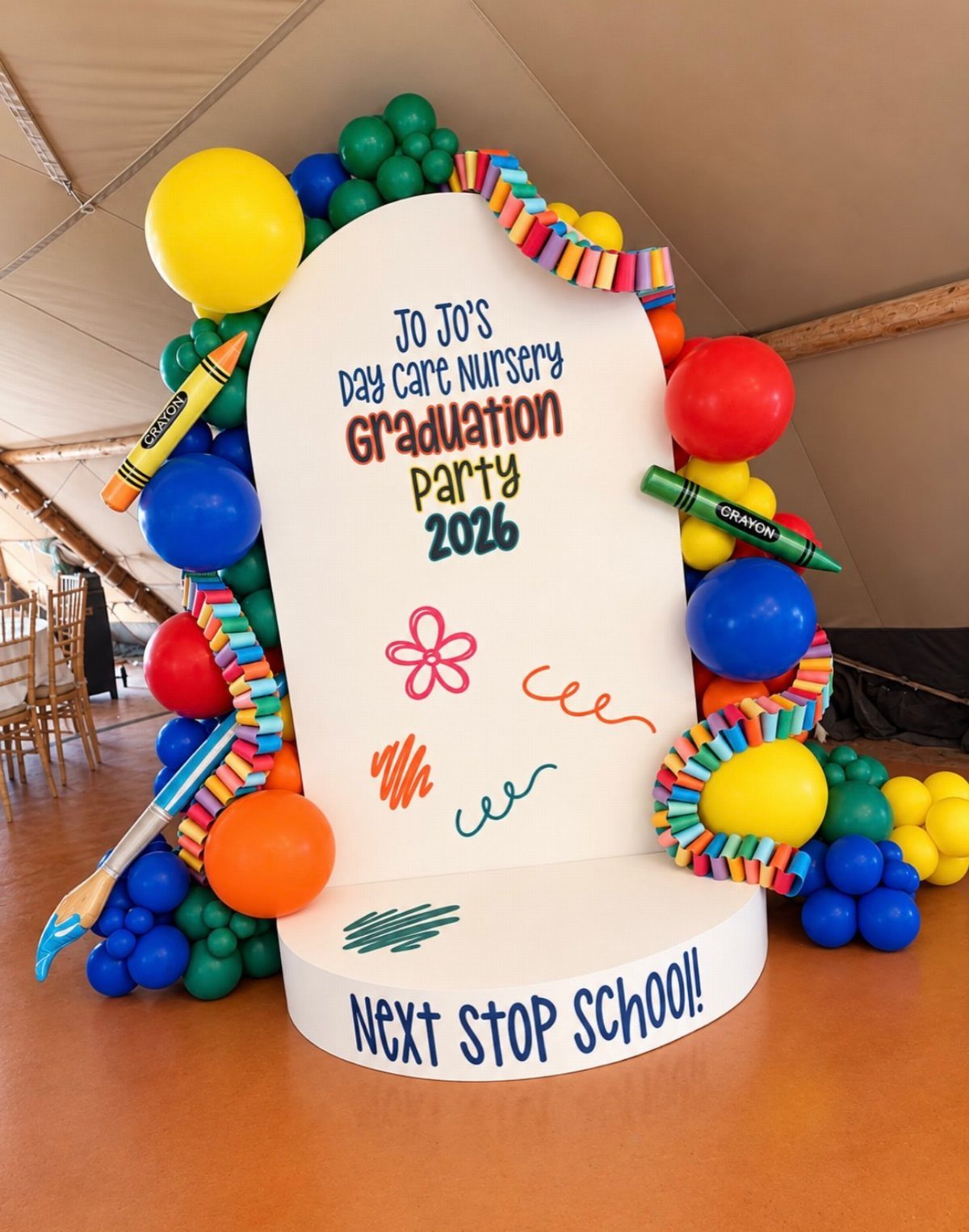Graduation party backdrop with colorful balloons, giant crayons, and celebratory nursery school text.