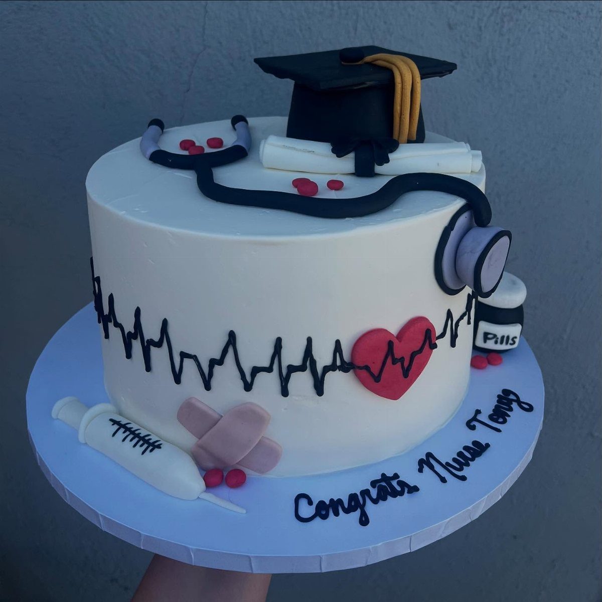 White nursing graduation cake with stethoscope, graduation cap, and EKG heart line.