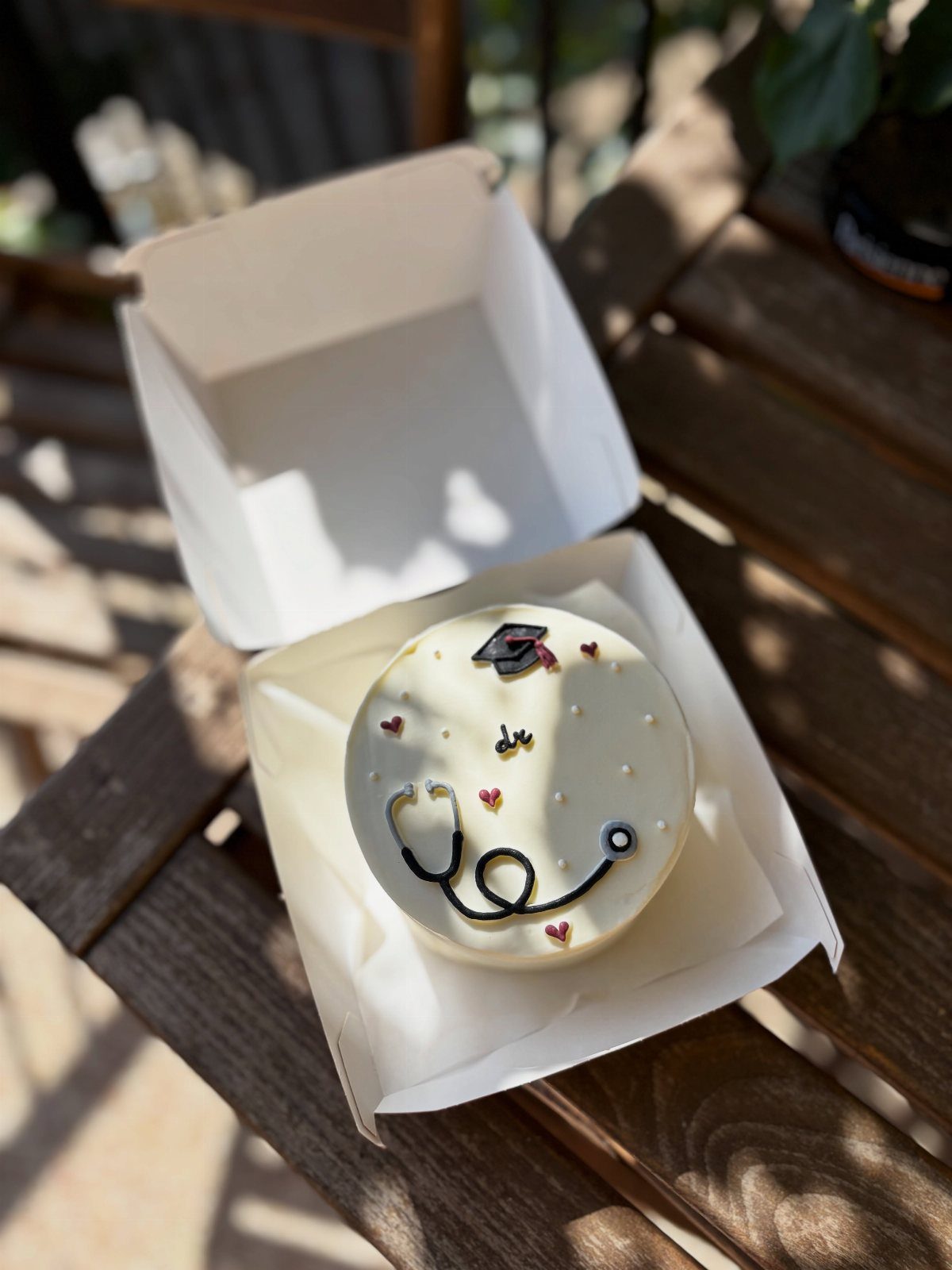 White frosted cake decorated with a black stethoscope and a graduation cap.