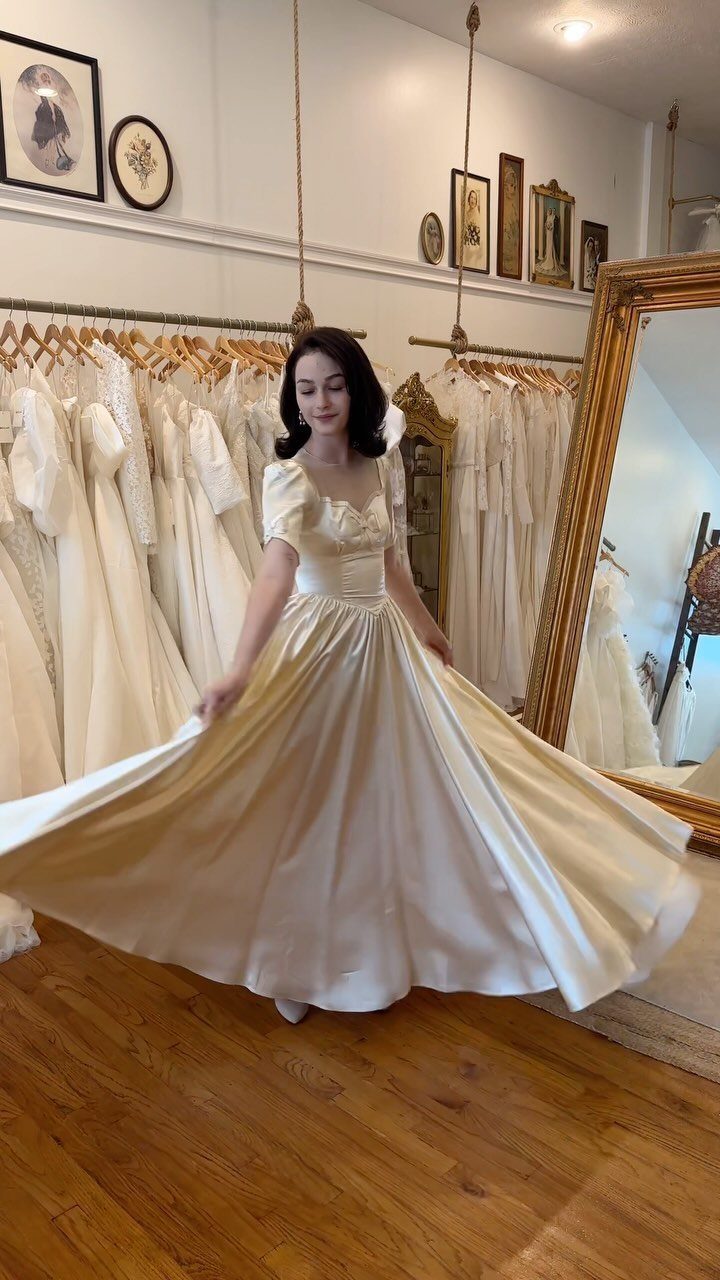 Woman in a cream satin ball gown posing in a bridal boutique.