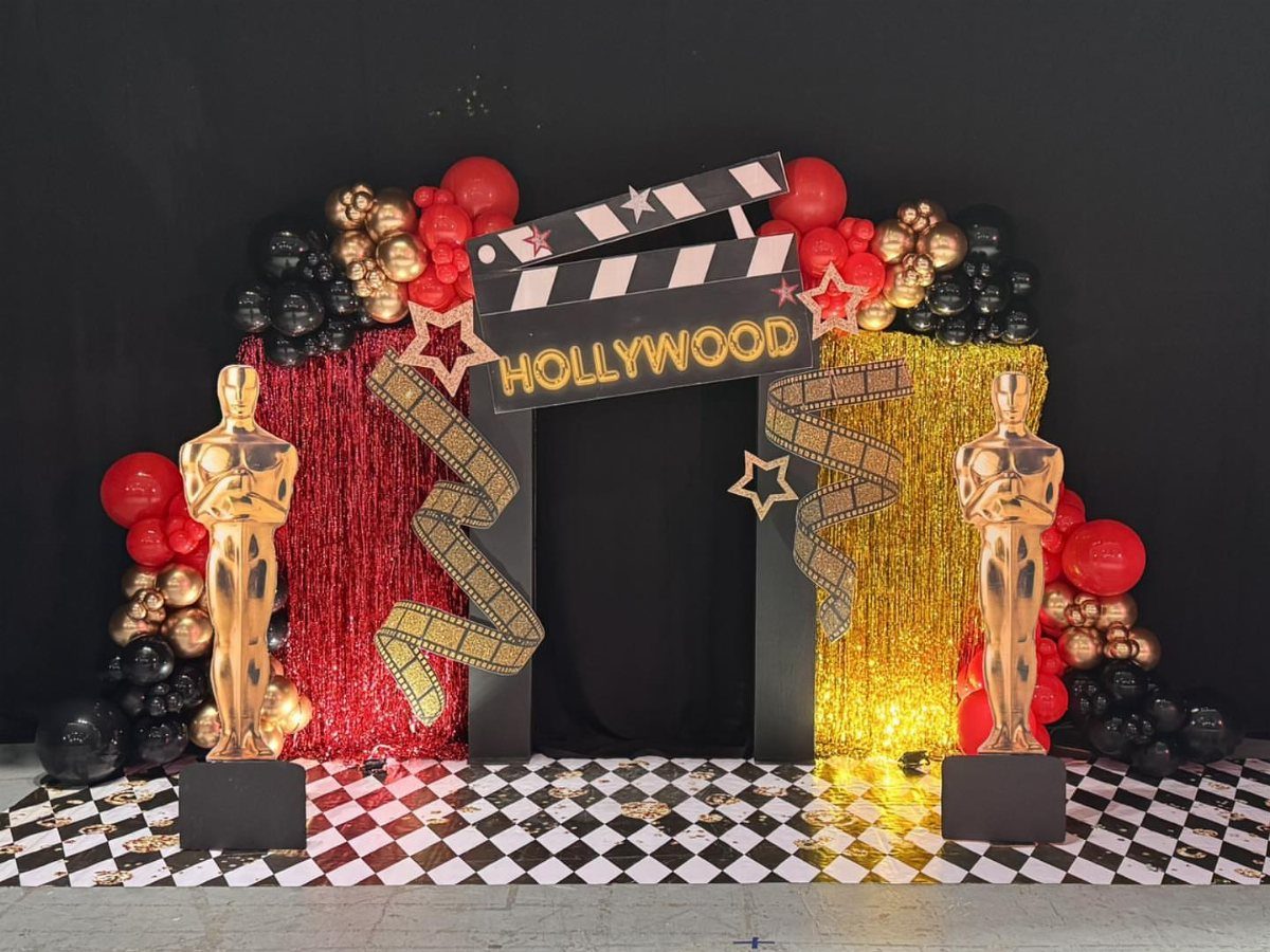 Hollywood themed photo backdrop with gold statues, red balloons, and movie clapperboard sign.