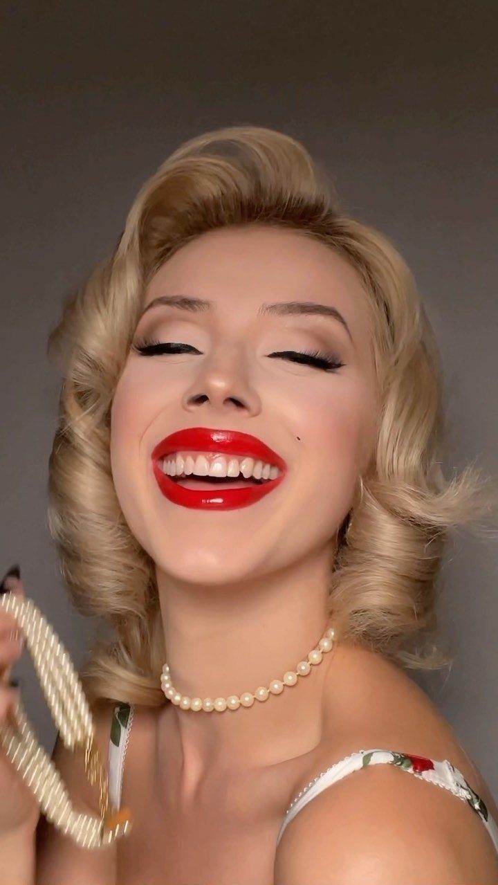 Blonde woman with vintage waves and bold red lips wearing a pearl necklace.