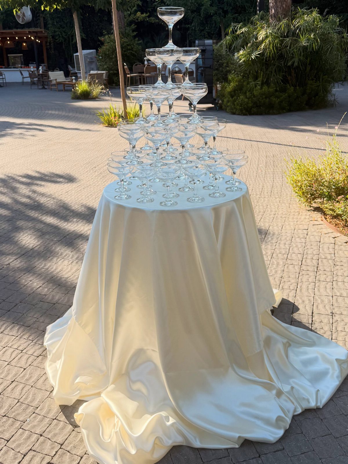 Champagne glass tower stacked in a pyramid on a cream satin draped table.