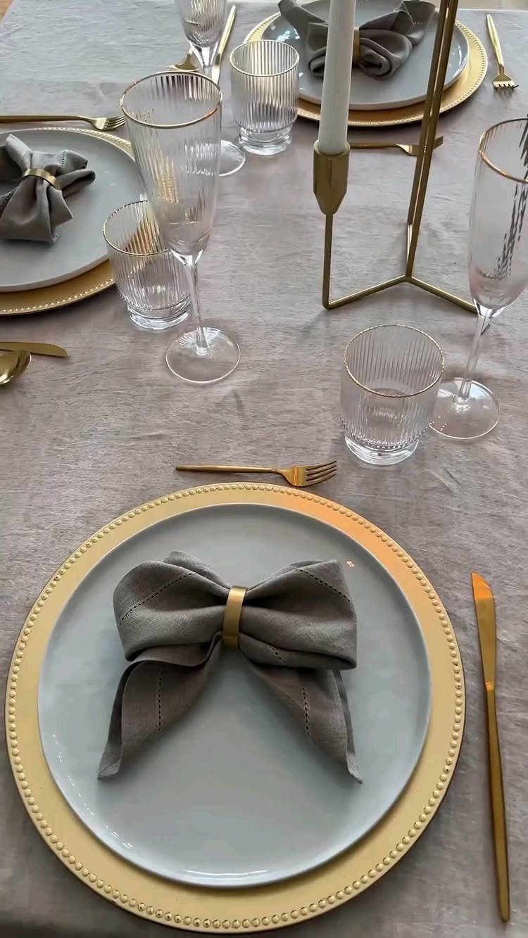 Grey napkins folded into bow ties on gold-rimmed plates for a formal dinner.