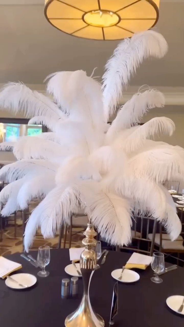 White ostrich feather centerpiece in a gold vase on a black dinner table.