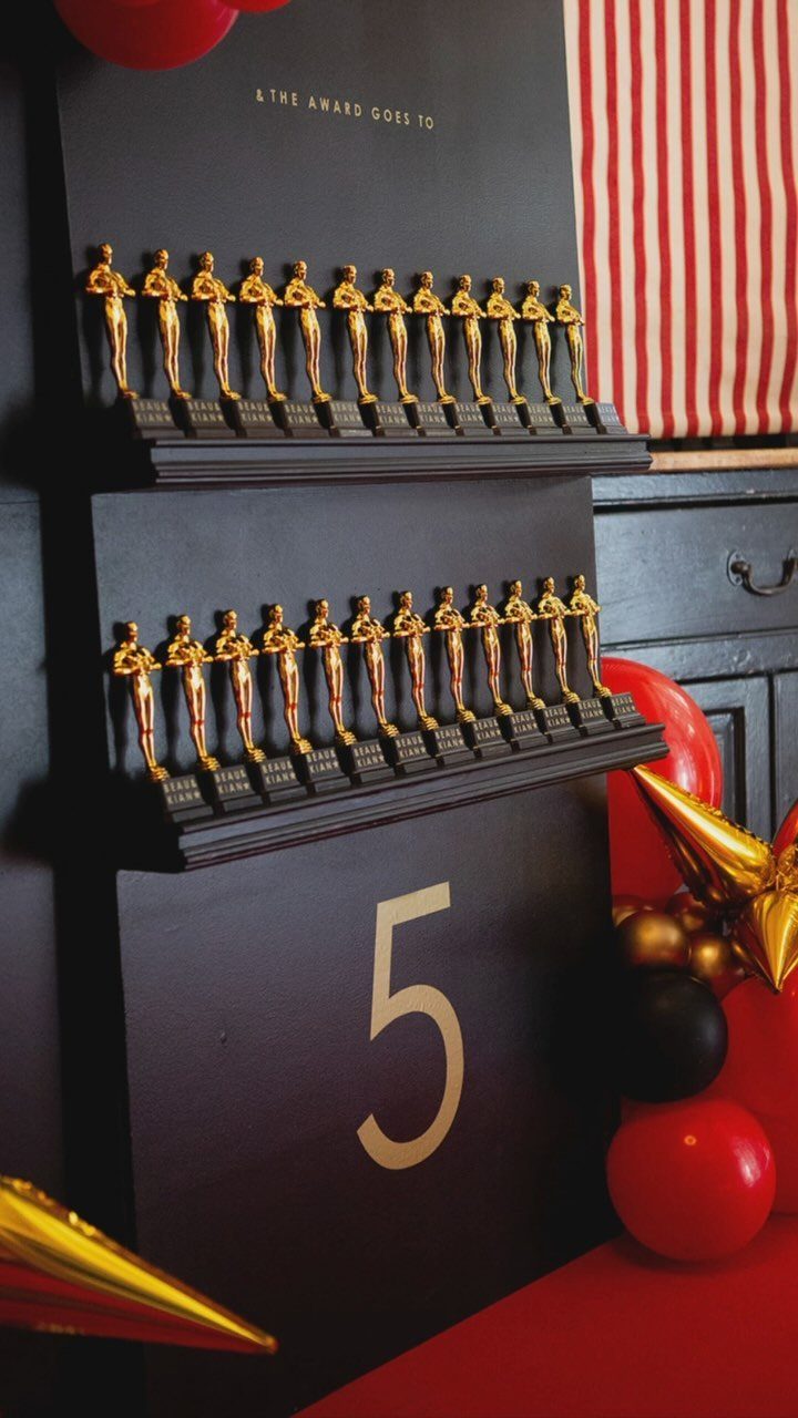 Gold award statues lined up on black shelves with red and black balloons.