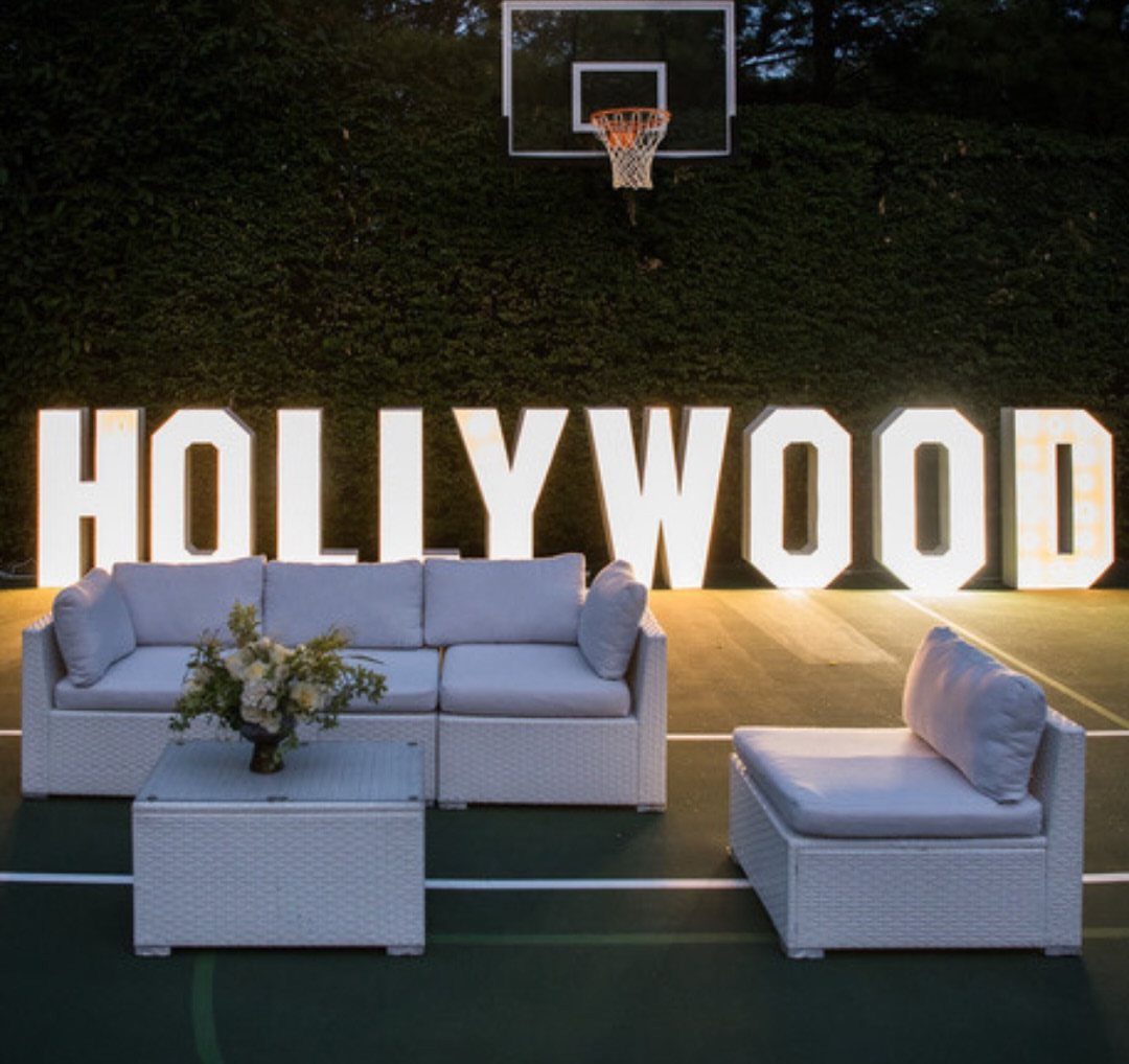 White wicker lounge furniture in front of large glowing HOLLYWOOD letters outdoors