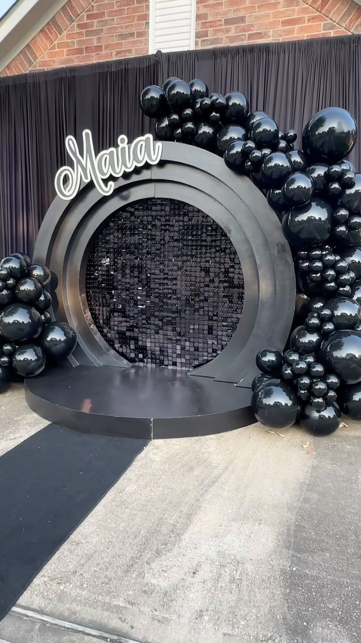 Black event backdrop with circular frame, sequins, black balloons, and Maia sign.