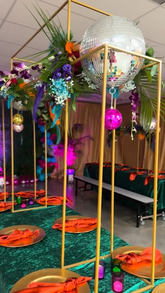 Decorated event table with gold geometric frame, disco ball, and tropical floral arrangements.