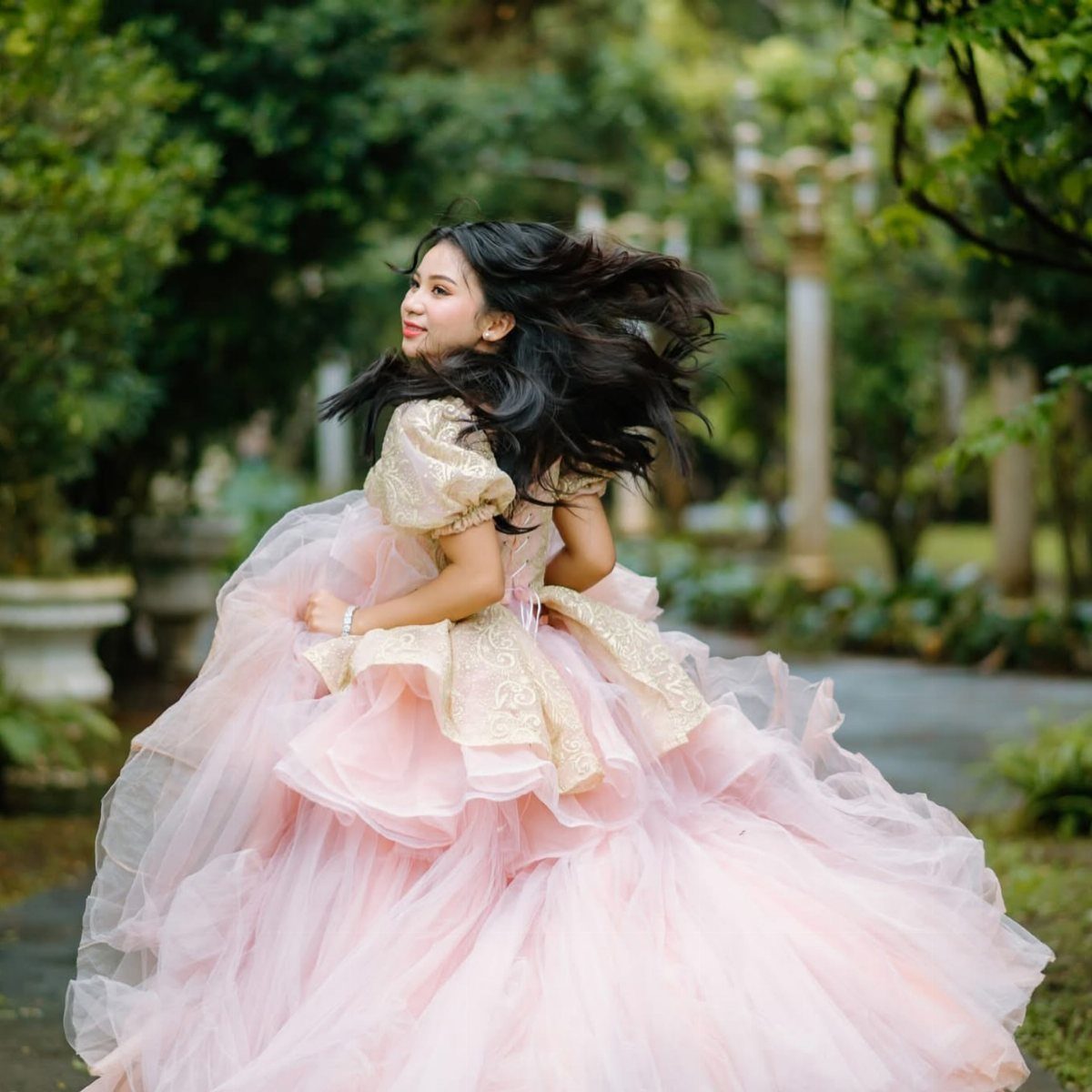 Woman in a pink and gold ballgown spinning in a green garden.