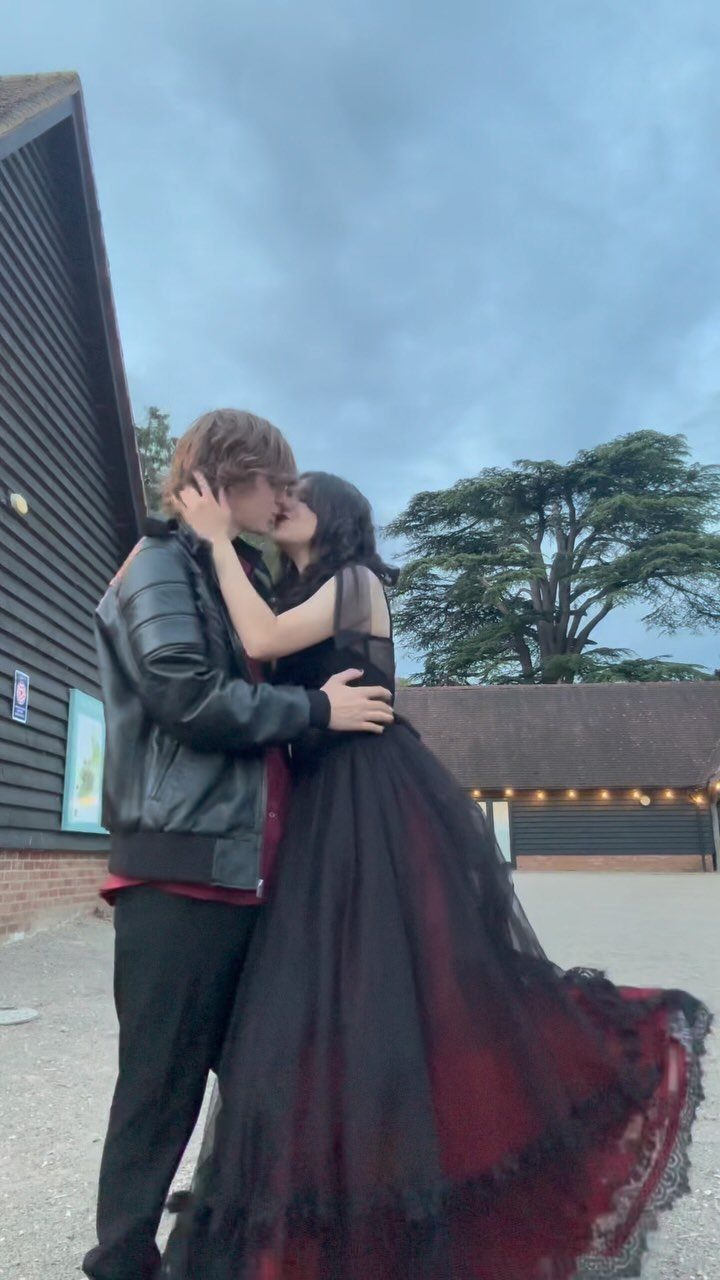 Couple kissing, woman in a black and red gothic ballgown, man in leather jacket.