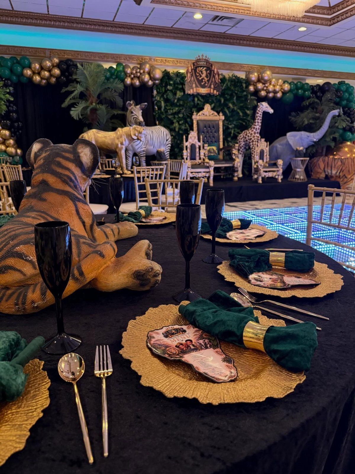 Safari themed banquet hall with animal statues, gold plates, and green balloons.