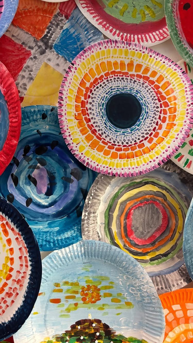 Painted paper plates with colorful abstract designs arranged in a collaborative art display.