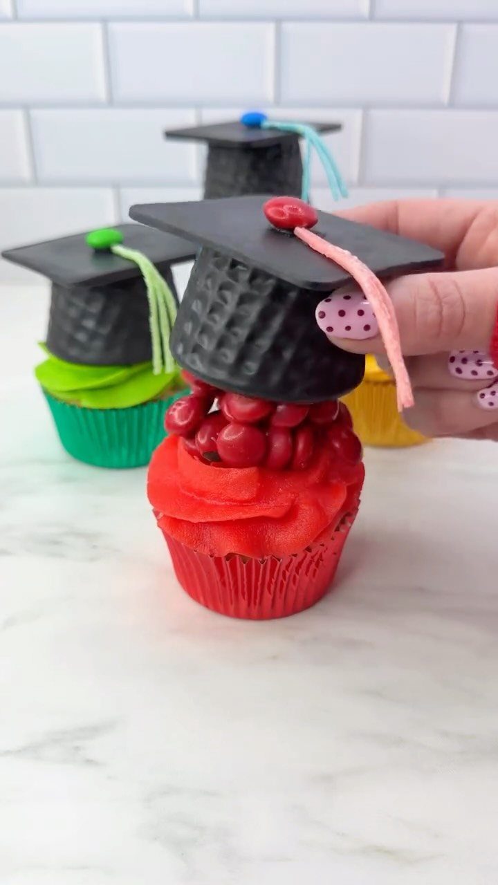 Graduation cap cupcakes with colorful frosting and black toppers on a white surface.