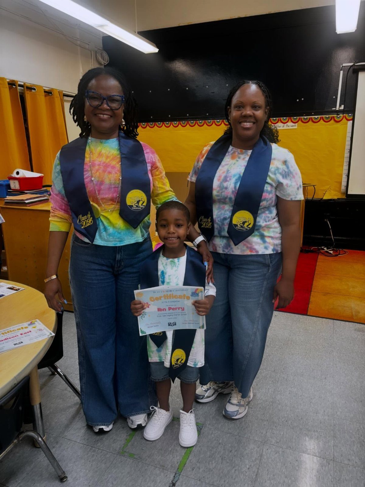 Two women and a young boy wearing graduation stoles and holding a certificate.