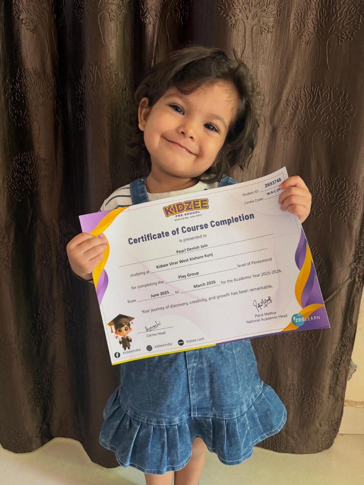 Young girl in denim dress smiling while holding a graduation course completion certificate.