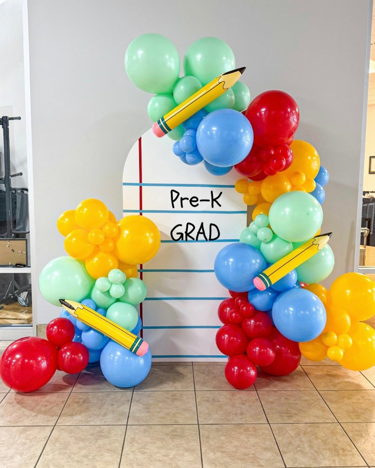 Colorful balloon arch with pencil props surrounding a Pre-K GRAD notebook backdrop.