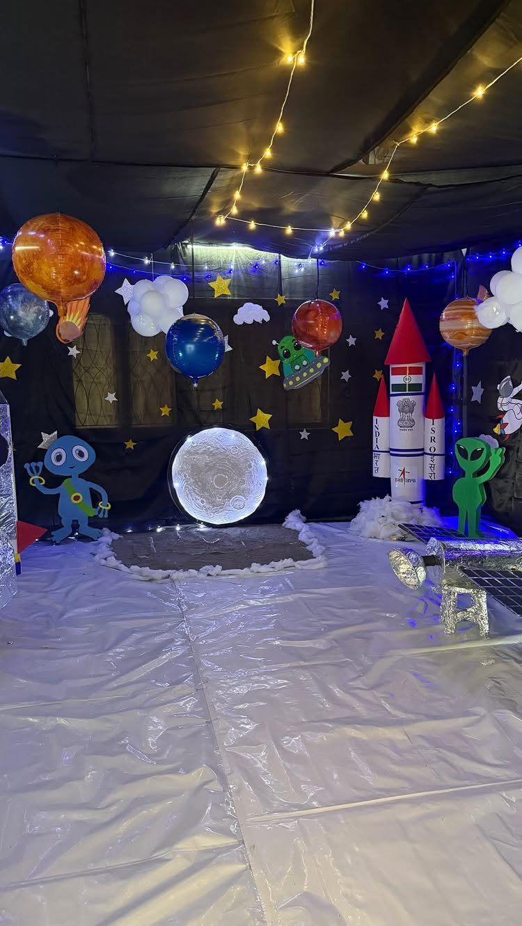 Space-themed party backdrop with a rocket ship, planet balloons, and alien figures.