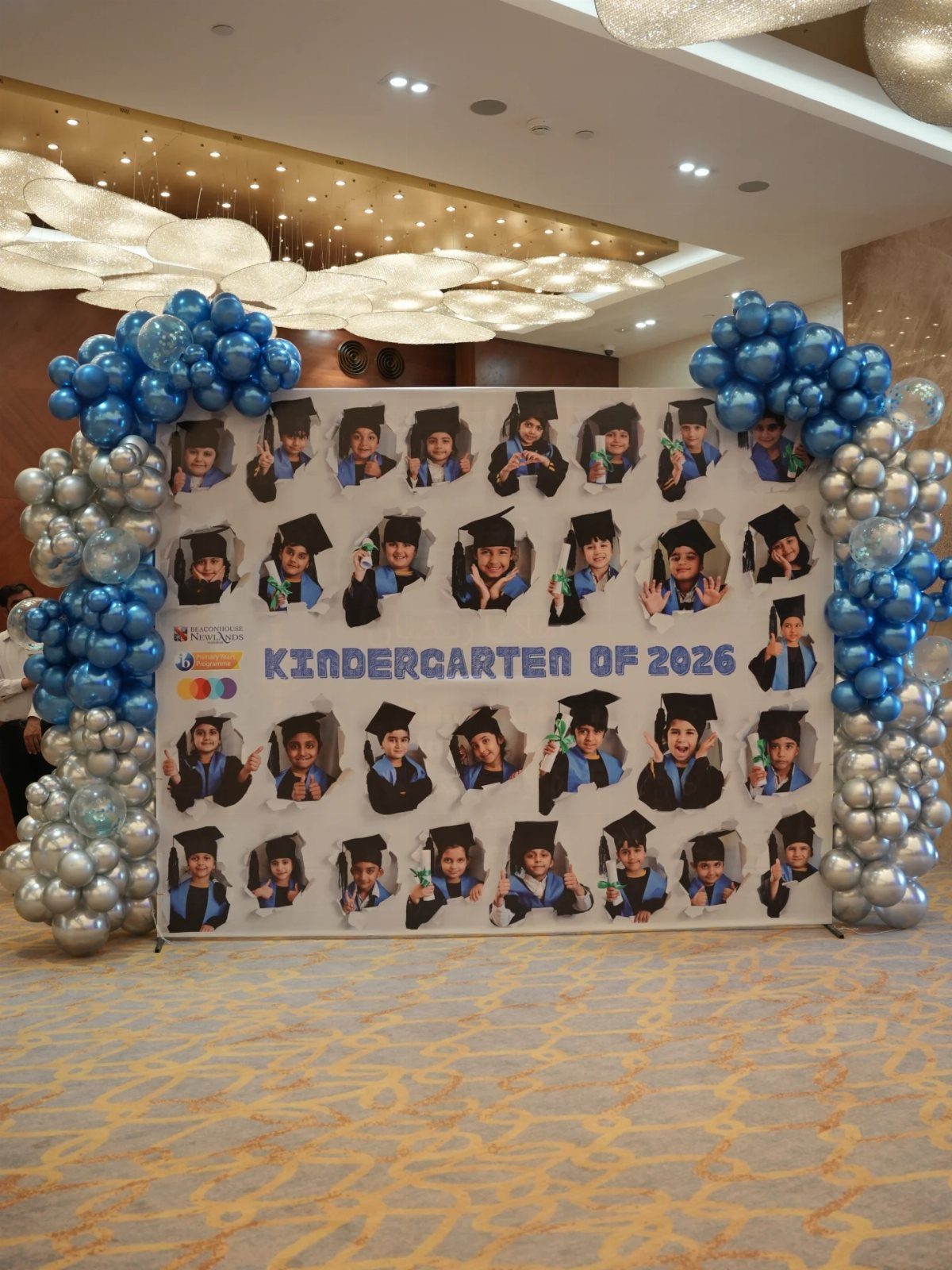 Graduation photo backdrop with children's faces in cut-outs and blue silver balloons