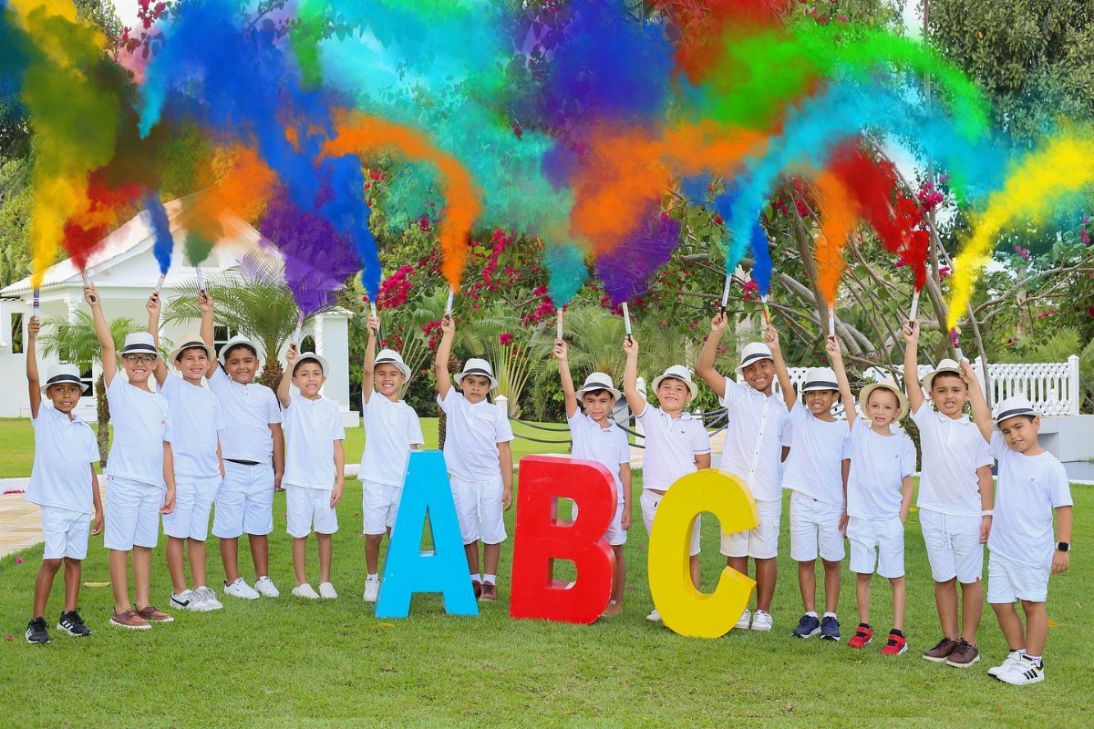 Young boys in white clothes posing with colorful smoke and large ABC letters.